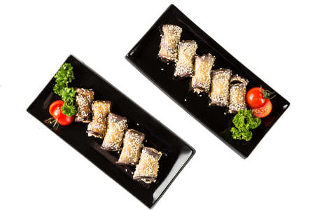 Eggplant rolls with cheese, garlic and sesame on black plates with herbs and tomato. Top view and isolated on whiteの写真素材