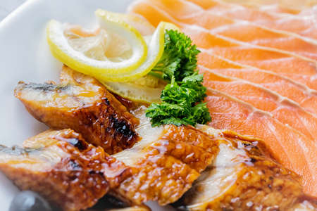 Raw salmon fillet pieces served with lemon, black olives and herbs on white plate close up with selective focus.の写真素材