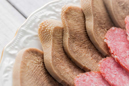 Boiled beef tongue on white plate close up with selective focus.