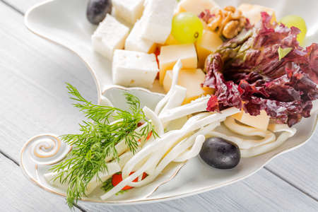 Restaurant cheese plate - various types of cheeses with grapes and black olive on white plate. Close up image with selective focus.の写真素材