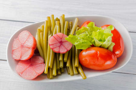 Pickled vegetables close up. Garlic, wild leek and tomato on white plate and wooden table. Top view.の写真素材