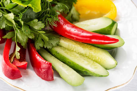 Vegetable slices with cucumber, tomatoes, paprika, lettuce, dill and herbs on white plate. Close up with selective focus.の写真素材