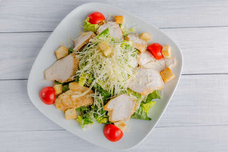 Healthy green organic caesar salad with cheese on white plate and wooden table. Top view.の写真素材