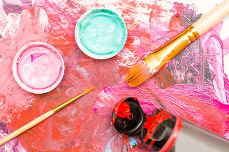 Painter workplace with tube of multicolor oil paint and paintbrushes on painted paper close up.