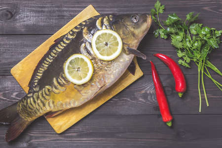 Mirror carp river fish with lemon, herbs and pepper on dark wooden table.の写真素材