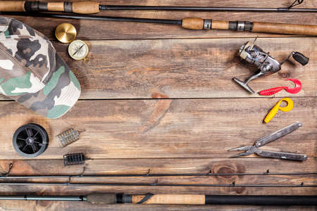 Fishing rods and reel with cap, fishing tackles, line and compass on wooden background with free space.の写真素材