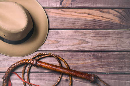 Travel and adventure concept. Vintage fedora hat and bullwhip on wooden table. Top view.