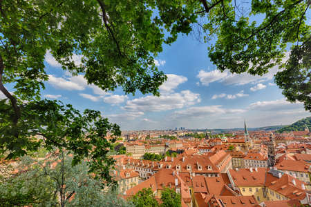 Houses with traditional red roofs and trees in Prague Mala Strana district in the Czech Republic. Trees and green leaves in the foreground.の写真素材