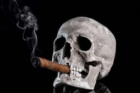 Close up portrait Skull with a cigar and smoke on black background. Health danger concept.の写真素材