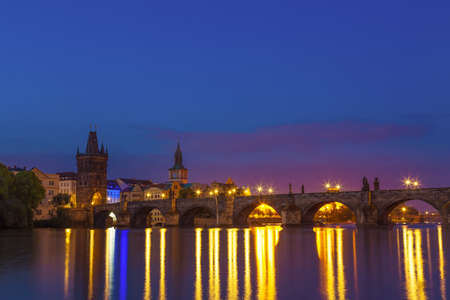 Charles bridge and riverbank with reflections in Prague, Czech republic during sunrise blue hour.の写真素材