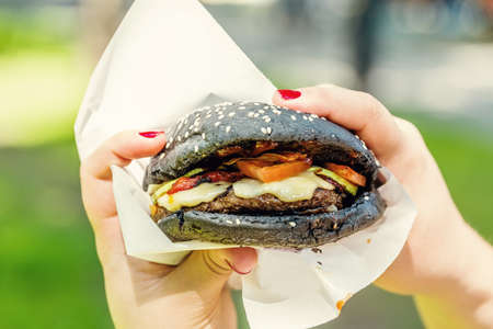 Woman hand holding tasty burger with black bread outdoors.の写真素材