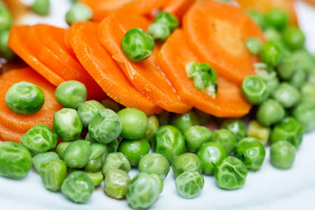 Boiled carrots and grean peas on white plate close up.の写真素材