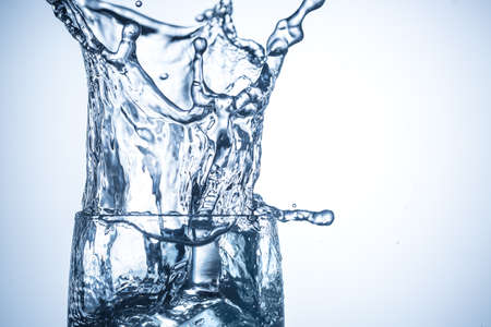 Ice cubes falling in glass with water splashes close up.の写真素材