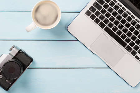 Retro photo camera, modern laptop computer and cup of cappuccino coffee on blue wooden background....