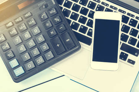 Business concept. Working desk with Laptop, calculator, modern phone and notebook on wooden table. Close up toned imageの写真素材