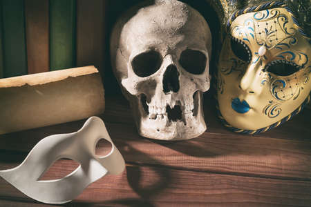 Theater and drama concept. Human skull, venetian masks with old scroll and books on wooden table.の写真素材