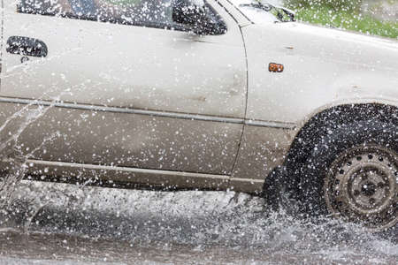 Car driving on a flooded road with water and splashes caused by heavy rainの写真素材
