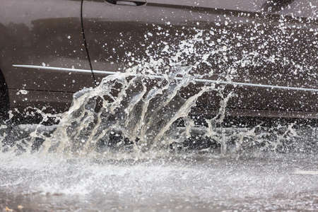 Car driving through a puddle on a flooded road with water and splashes caused by heavy rainの写真素材