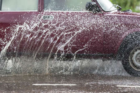 Car driving through a puddle on a flooded road with water and splashes caused by heavy rainの写真素材