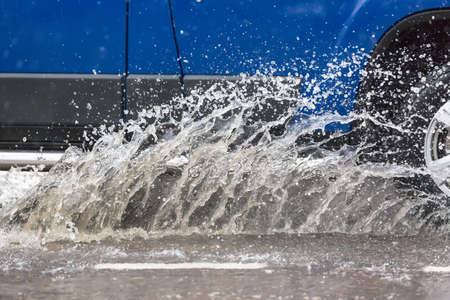 Car driving through a puddle on a flooded road with water and splashes caused by heavy rainの写真素材