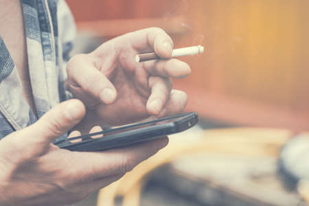 Man hand holding smoking cigarette and using mobile smart phone. Tonedの写真素材