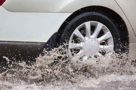 Car driving through a puddle on a flooded road with water and splashes caused by heavy rainの写真素材