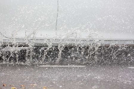 Car motion through big puddle of water splashes from the wheels on the street roadの写真素材