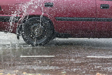 Car motion through big puddle of water splashes from the wheels on the street roadの写真素材