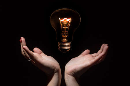 Idea and success coincept. Glowing light bulb without wires and opened female hands on black backgroundの写真素材
