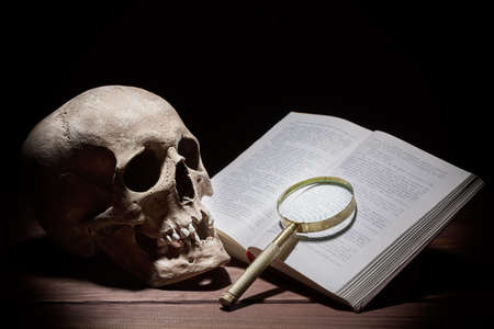Human skull near old open book and magnifying glass on black backgroundの写真素材