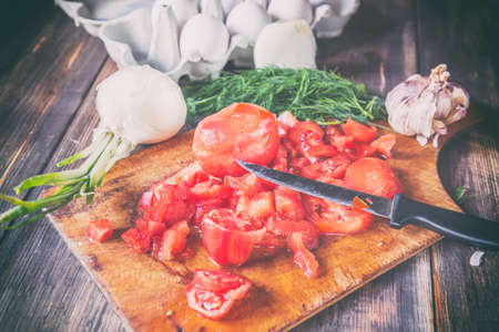 Omelette preparation with cut tomatoes, dill, onion, eggs and knife. Toned imageの写真素材