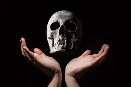 Black magic concept. Human skull between woman hands on black backgroundの写真素材