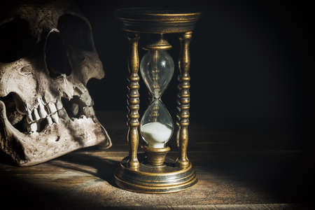 Skull and vintage hourglass on wooden background under beam of light.