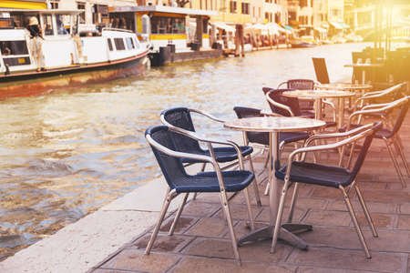 Restaurant tables and chairs with vaporetto ships in the background in Venice, Italy. European travel, outdoor dining and cuisineの写真素材