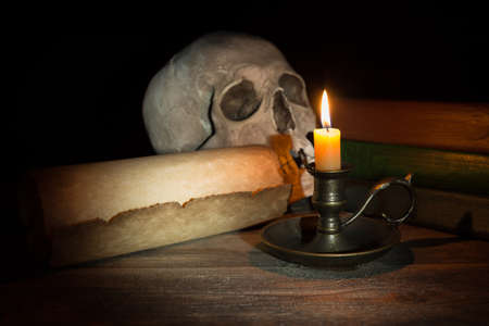 Burning candle in candlestick near old book and vintage scroll on black background.の写真素材