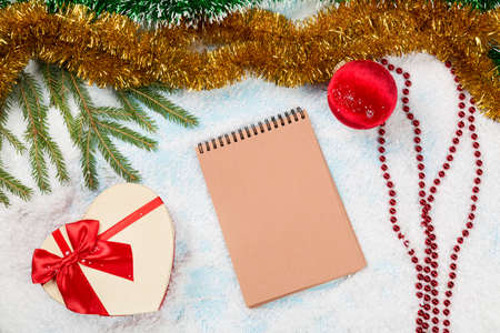 Message to Santa Claus. Christmas fir tree branches on wooden board with blank notebook with spangle, christmas ball and giftbox on snow. Christmas or new year frame for your project with copy space on the blank notebookの写真素材