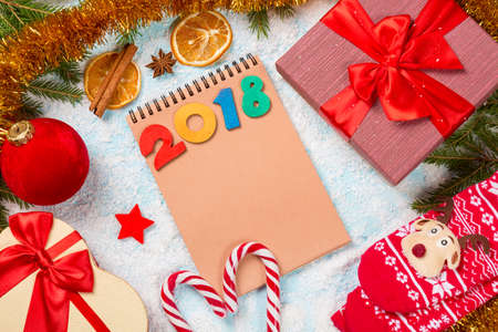 Christmas decoration card with fir tree, gift-boxes, spangle, star, cinnamon, orange, christmas sock and candy canes on snow background with blank notebook and 2018 decorative numbers.の写真素材