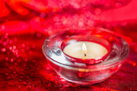 Burning red tea light candle on Christmas decoration colorful glitter red bokeh background.の写真素材