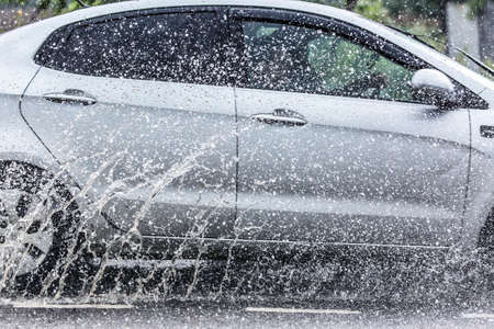 Car splashes through a large puddle on a flooded street during heavy rain. Nature disaster.