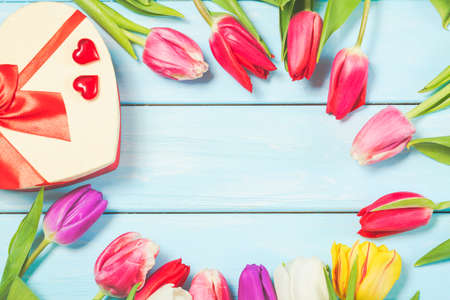 Colorful spring tulip flowers with decorative giftbox and hearts on light blue wooden background as greeting card with free space. Mothersday or spring conceptの写真素材