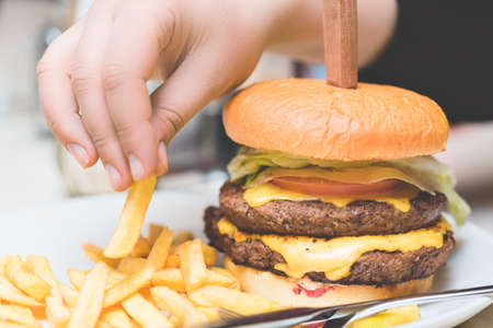 Fast food concept. Female hand taking french fries near big fresh burger. Close up image.の写真素材