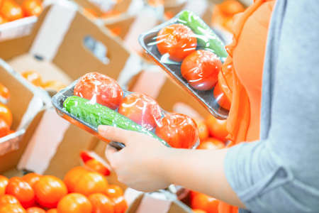 Woman in a supermarket at the vegetable shelf shopping for tomatoes and cucumbers. Shopping conceptの写真素材