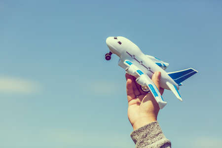 Toy plastic airplane in hand against blue sky. Dreams, vacation or travel concept. Vintage toned...