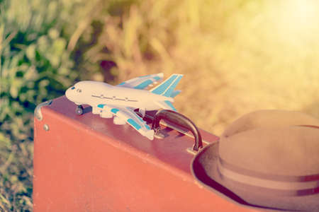 Travel and adventure concept. Vintage brown suitcase and hat with toy airplane in the green field....