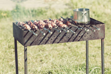 Fresh grilled meat on skewers and outdoor grill with cooking pot outdoors. Toned