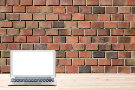 Conceptual workspace or business concept. Laptop computer with blank white screen on light wooden table against red brick wall or backgroundの写真素材