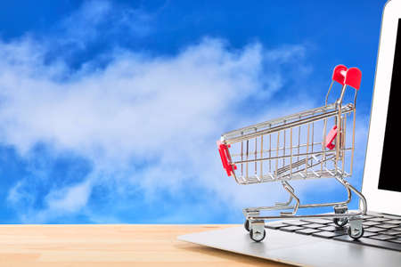 Red shopping cart on a laptop against blue sky background. Online internet shopping conceptの写真素材