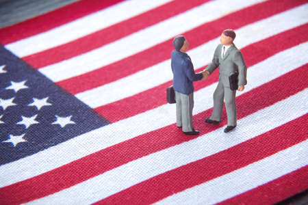 Business deal or agreement and success concept. Two miniature businessmen shaking hands while...