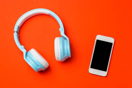 Blue modern wireless headphones with a mobile phone on red orange background. Listening to music conceptの写真素材