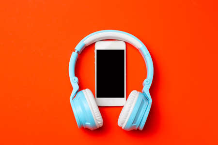 Blue modern wireless headphones with a mobile phone on red orange background. Listening to music conceptの写真素材